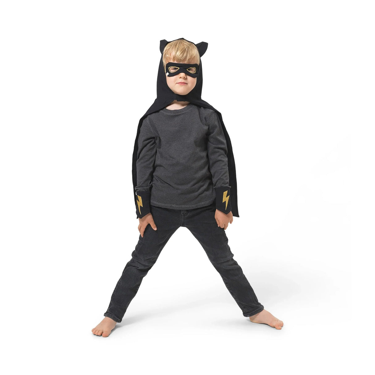 Kind mit schwarzem Superhelden-Kostüm, Maske und Blitzsymbol auf Armstulpen vor weißem Hintergrund