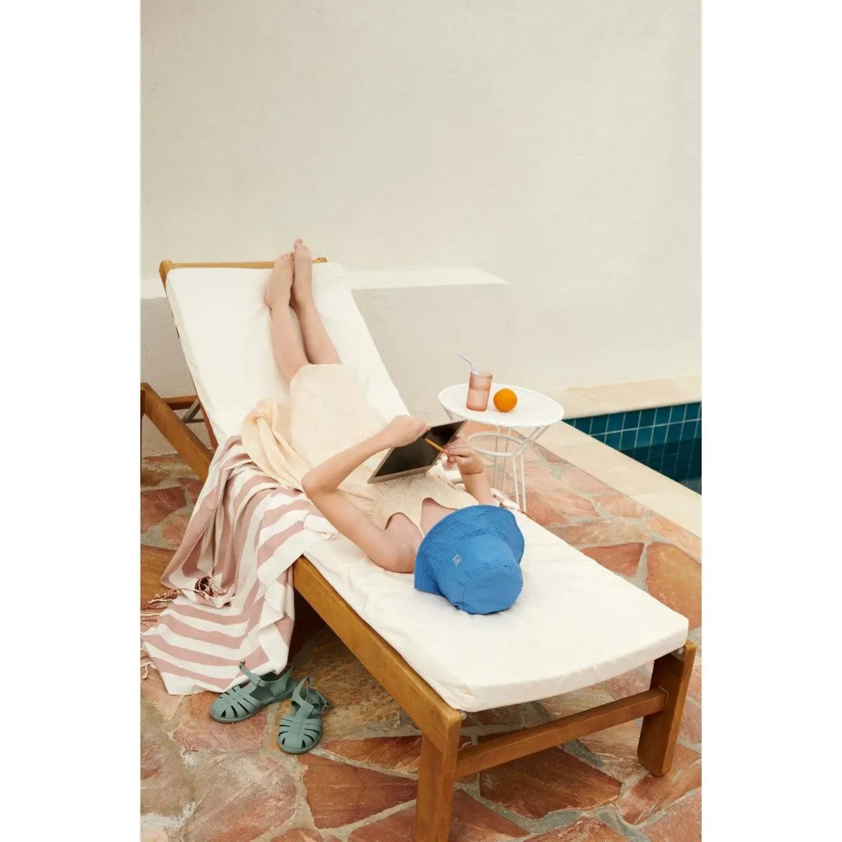 Kind liegt auf Liege am Pool, liest Tablet, Sommertag, Relaxen, Sonnenhut, Outdoor