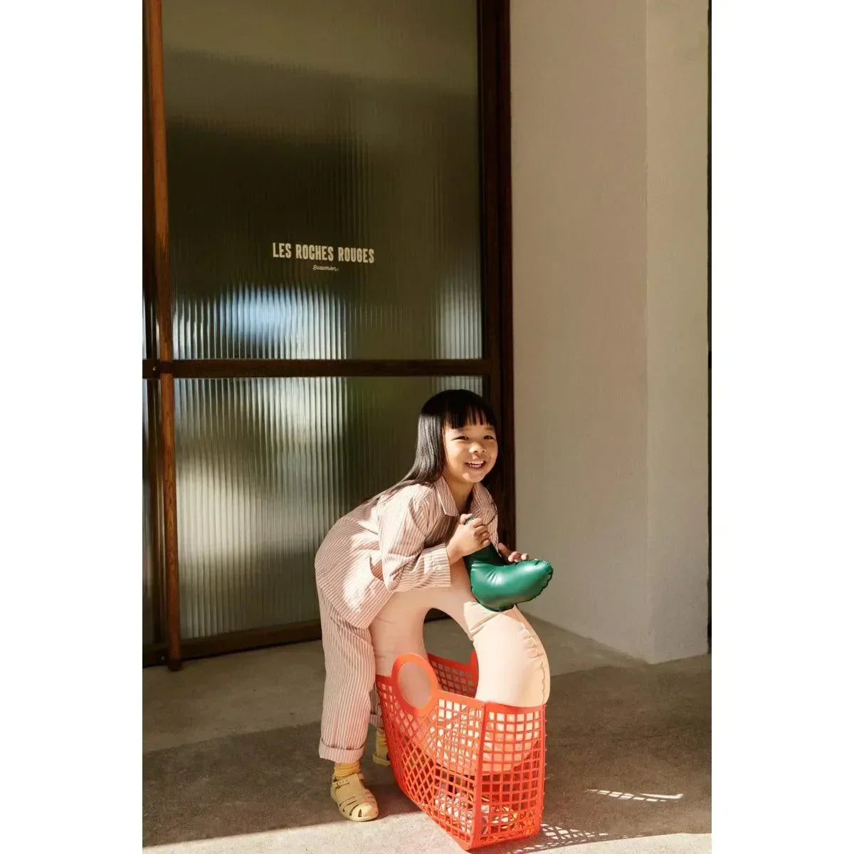 Mädchen mit orangefarbener Kinderkorb-Tasche und aufblasbarem Tier-Spielzeug, sonniger Eingangsbereich
