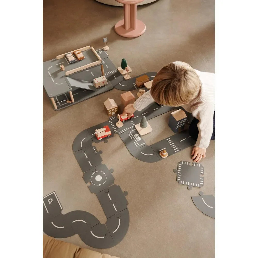 Kind spielt mit Holzautos und Straßenset auf dem Boden im Kinderzimmer