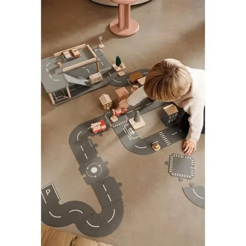 Kind spielt mit Holzautos und Straßenset auf Kinderzimmerboden, pädagogisches Spielzeug