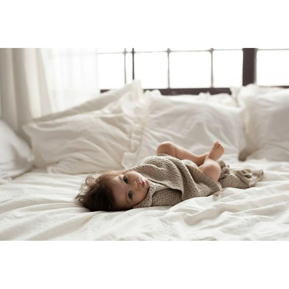Kleinkind liegt im Bett und ist in einer Bambus-Babydecke gewickelt