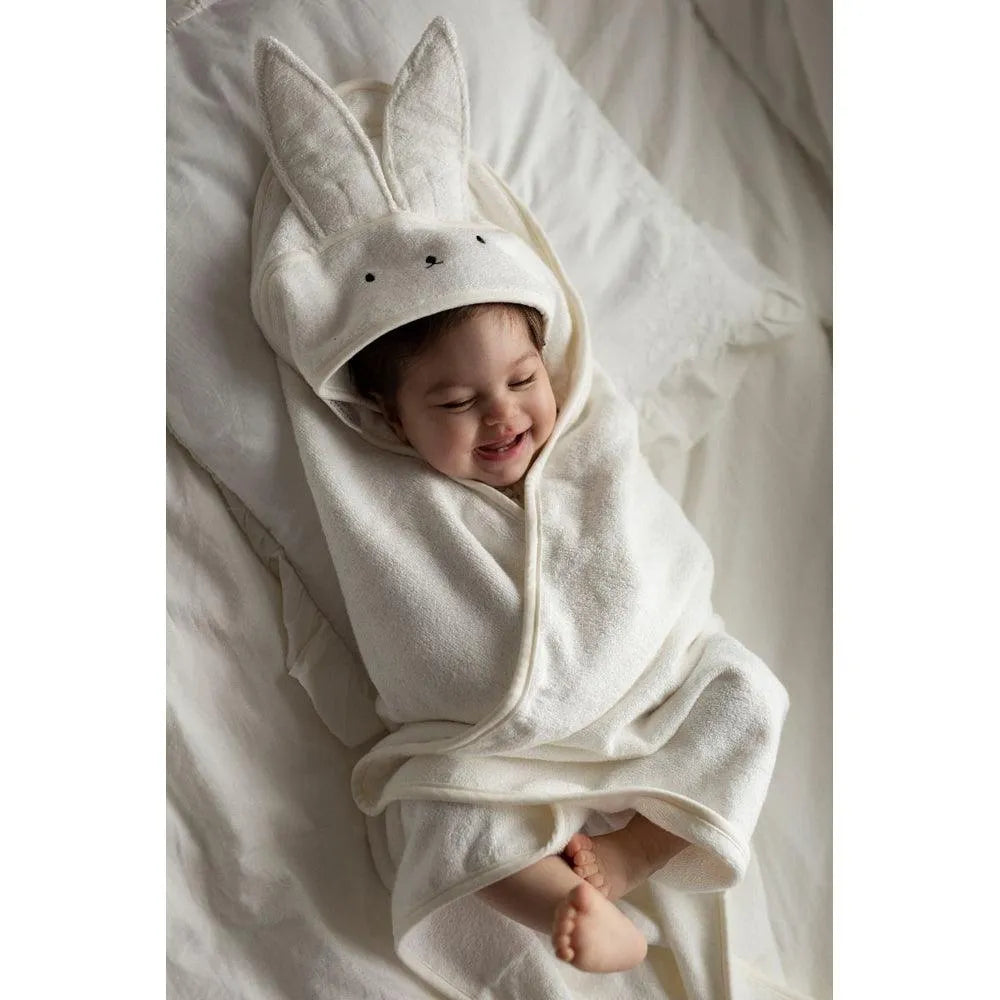 Ein lächelndes Baby, das in einem Kapuzenhandtuch von My Memi nach dem Baden eingewickelt ist.
