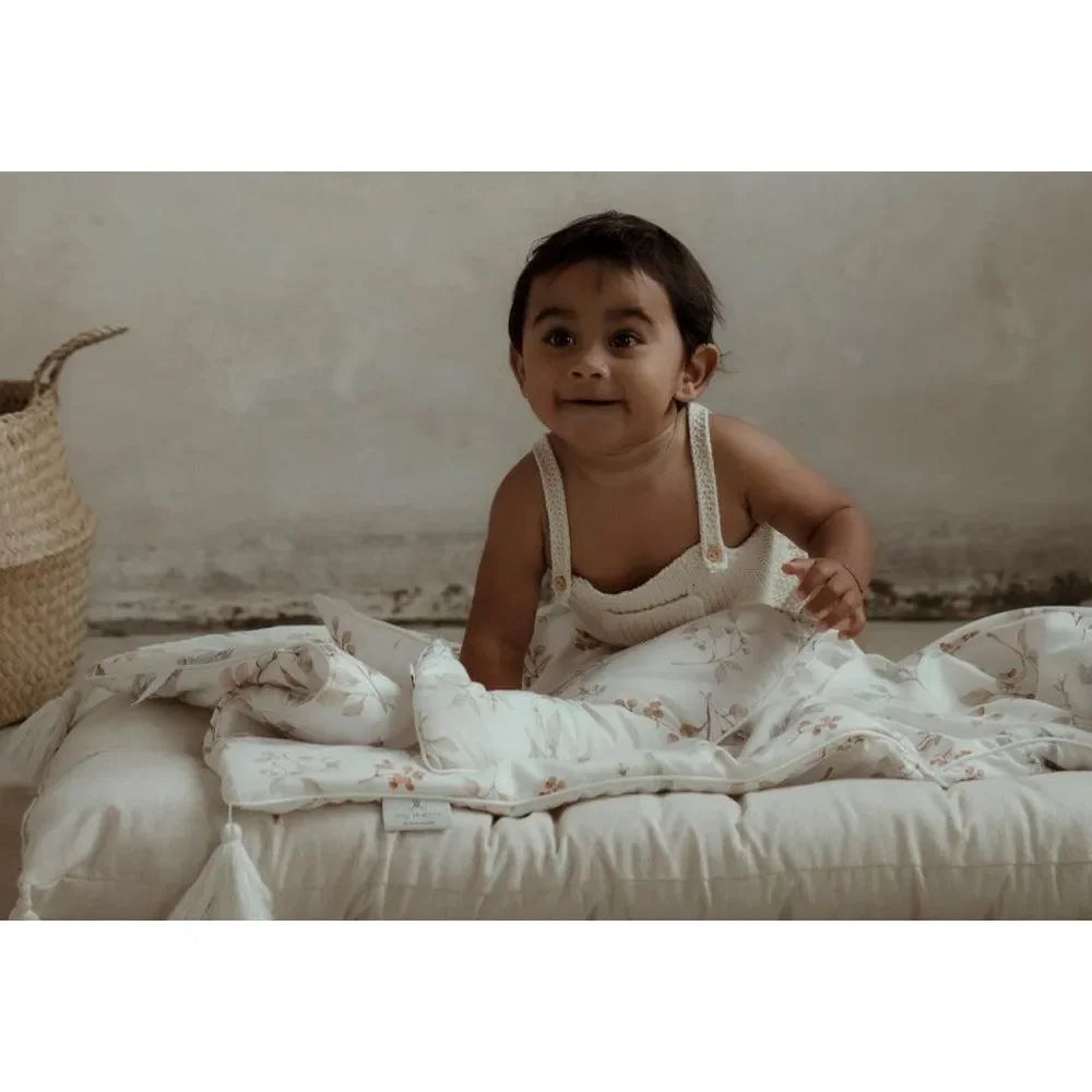 Baby auf gepolsterter Unterlage mit floralem Bambus-Wickeltuch in natürlichem Setting