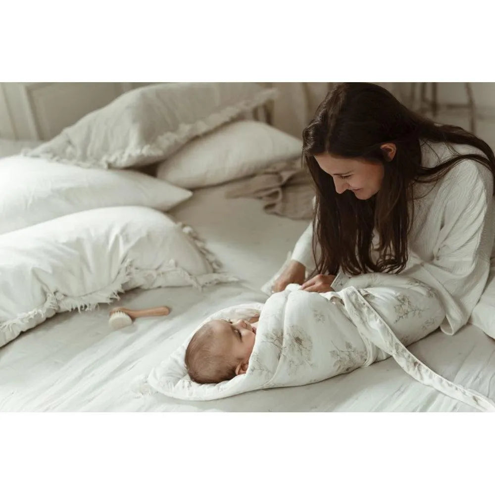 Mutter wickelt ihr Baby auf dem Bett in einer My Memi - Bambus Babydecke / Wickeldecke