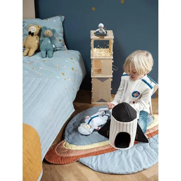 Kind spielt auf gesteppter Babydecke im Planeten-Design mit Kuscheltier-Rakete im Kinderzimmer