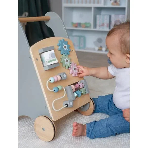 Baby spielt mit Holz-Lauflernwagen mit Motorikspielzeug im Kinderzimmer