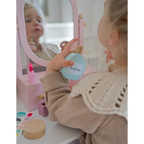Kind spielt mit Schminkkoffer am Schminktisch, hält Spielzeug-Parfümflasche in der Hand