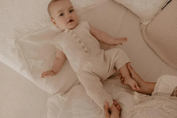Baby im beigen Strick-Jumpsuit liegt auf einem Bett, gemütliche Kinderzimmer Atmosphäre
