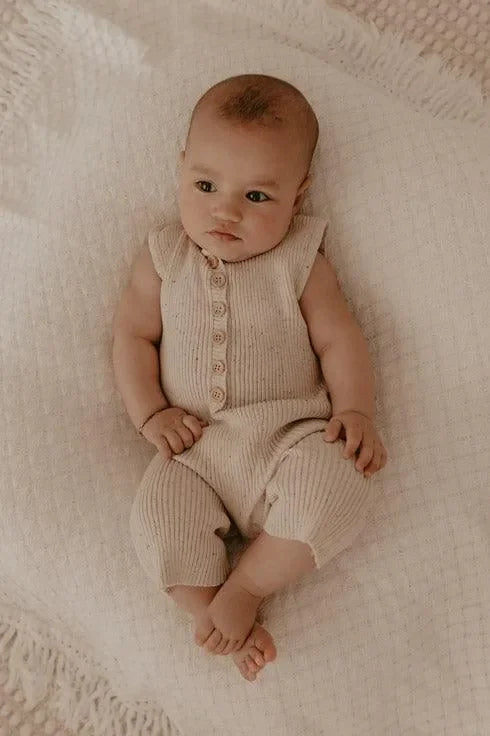 Baby in beigem Strick-Jumpsuit auf weicher Decke, gemütliche Babymode