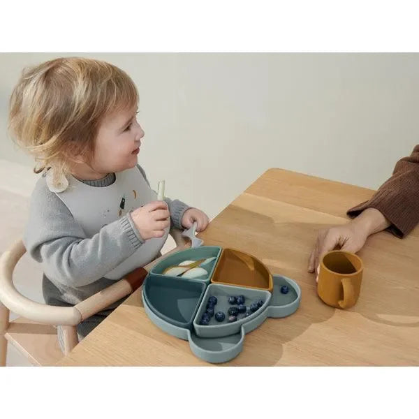 Kind sitzt am Tisch mit einem geteilten Silikonteller in Bärenform und isst Obst
