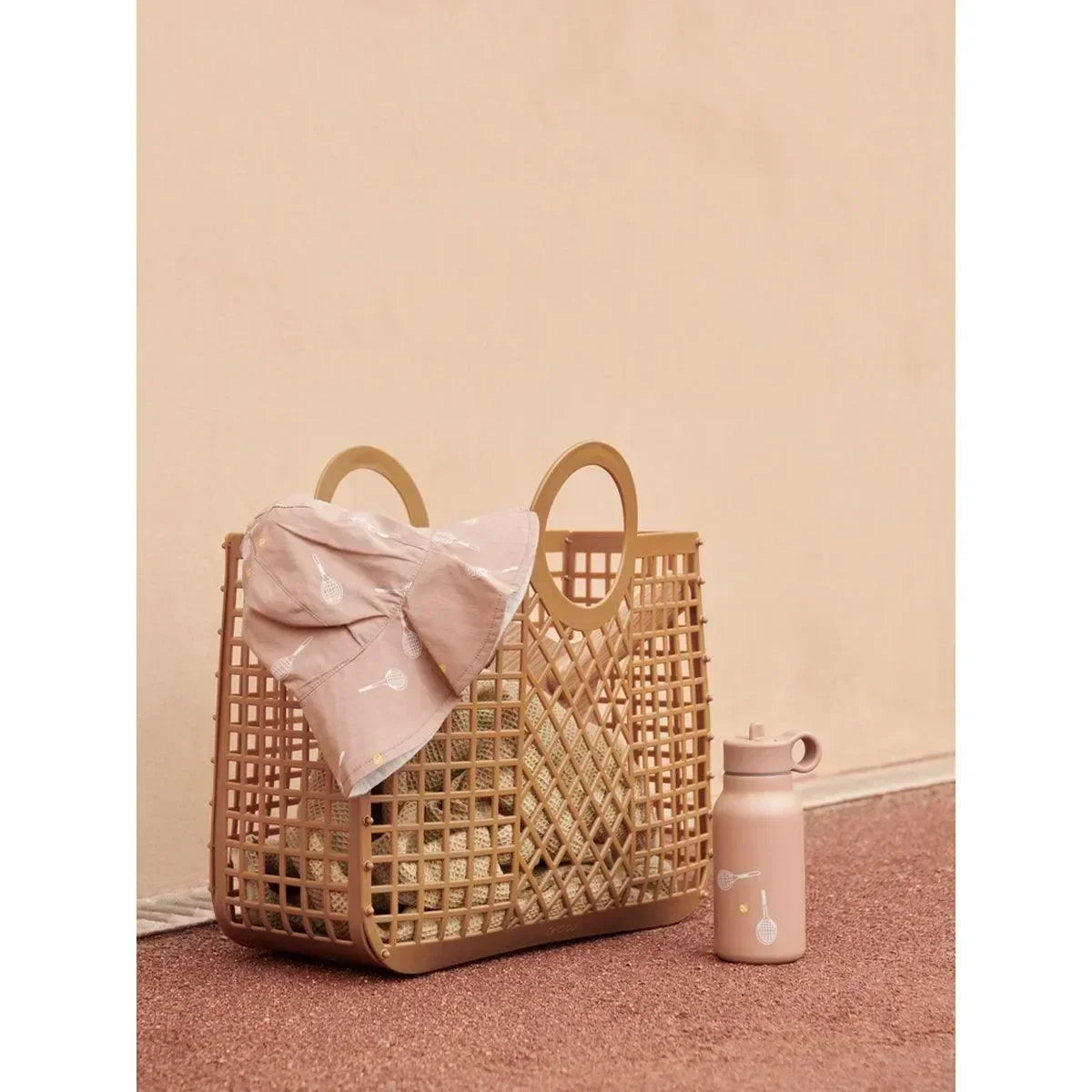 Beige Kinderkorb mit runden Griffen, rosa Sonnenhut und Trinkflasche auf rosa Boden