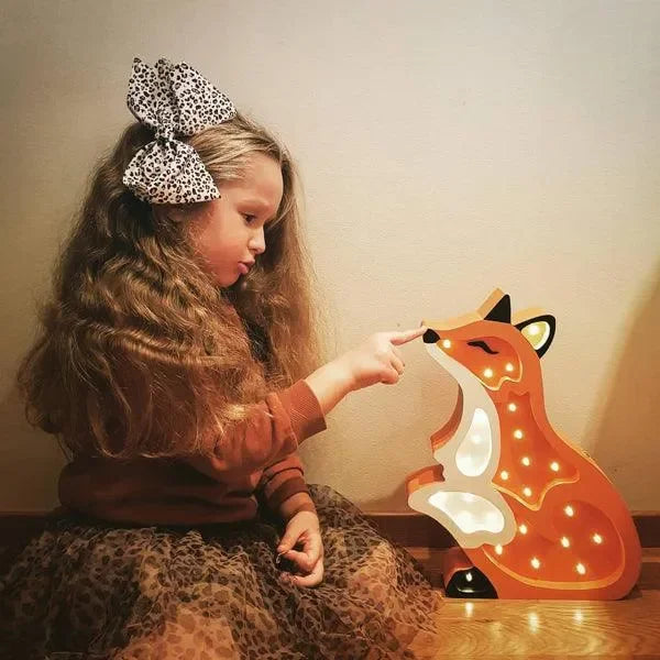 Mädchen sitzt neben leuchtender LED-Fuchs-Kinderzimmerlampe im warmen Kinderzimmer