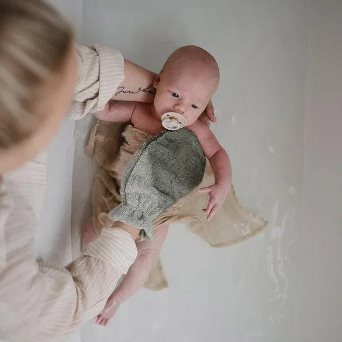 Baby beim Baden mit grauem Waschhandschuh in Fischform, sanfte Babypflege