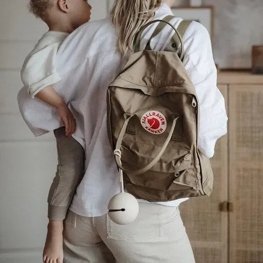 Beige Schnullertasche am Rucksack, Mutter trägt Kleinkind in heller Wohnung
