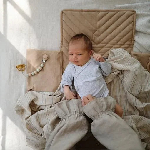Baby auf tragbarer Wickelunterlage in Naturfarbe mit Kuscheldecke und Schnuller