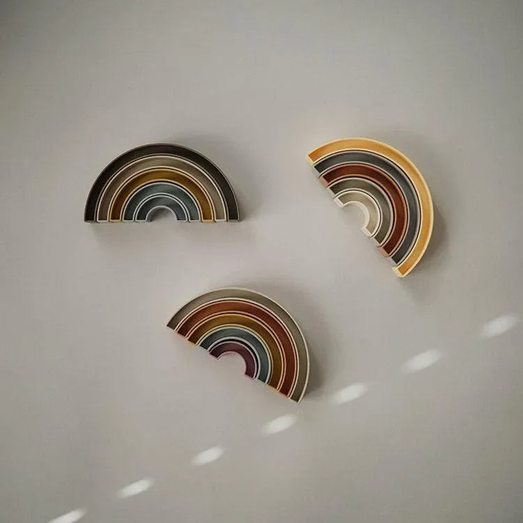 Drei stapelbare Regenbogen Holzspielzeuge in sanften Farben auf hellem Hintergrund