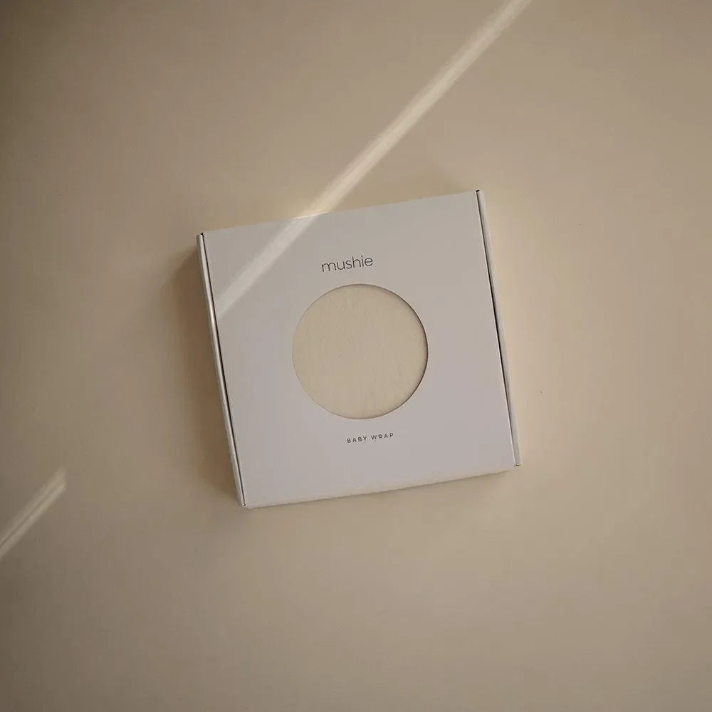 Beigefarbene Babytrage in minimalistischer Verpackung auf hellem Hintergrund