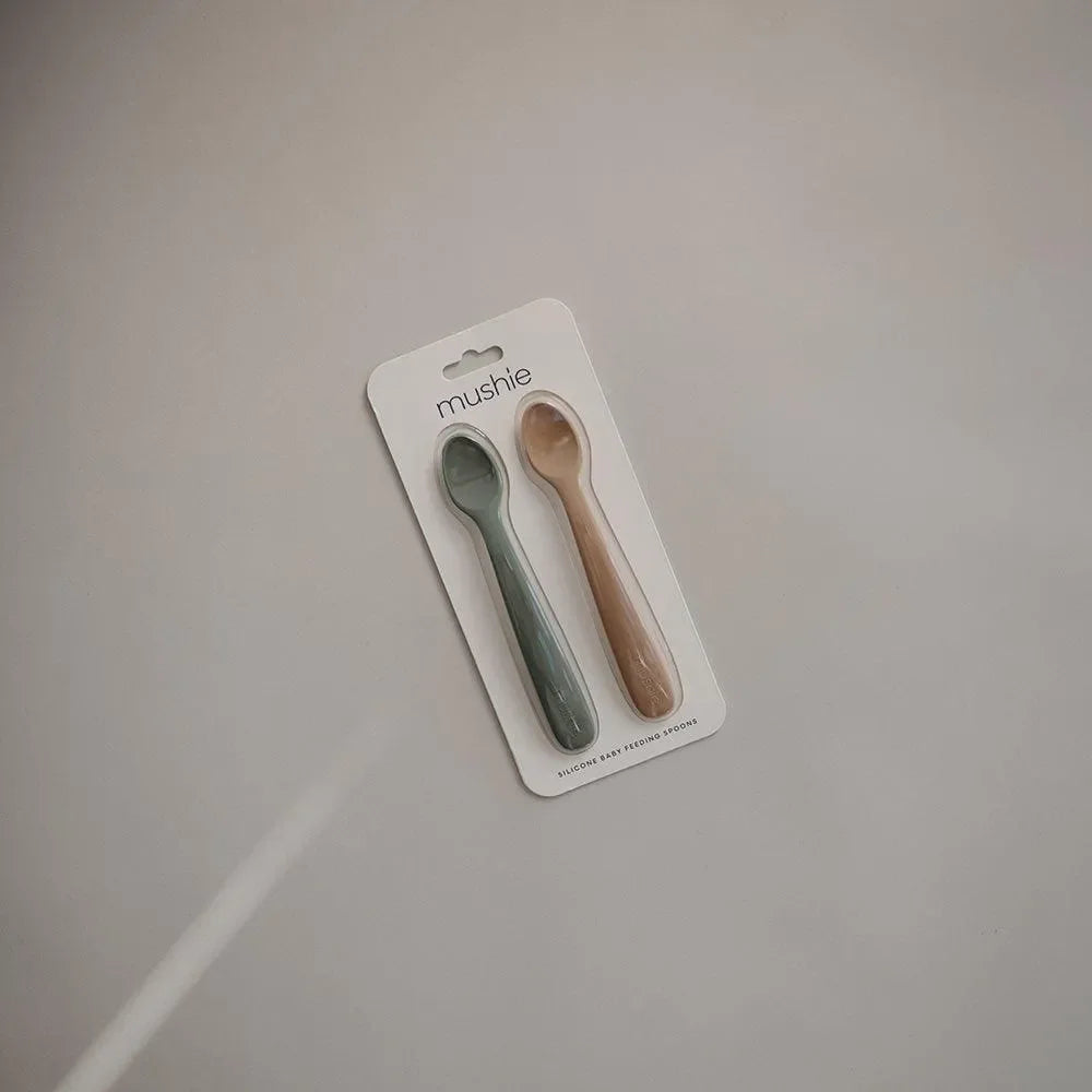 Zwei Baby-Löffel aus Silikon in grün und mauve auf neutralem Hintergrund, auf Karte verpackt.