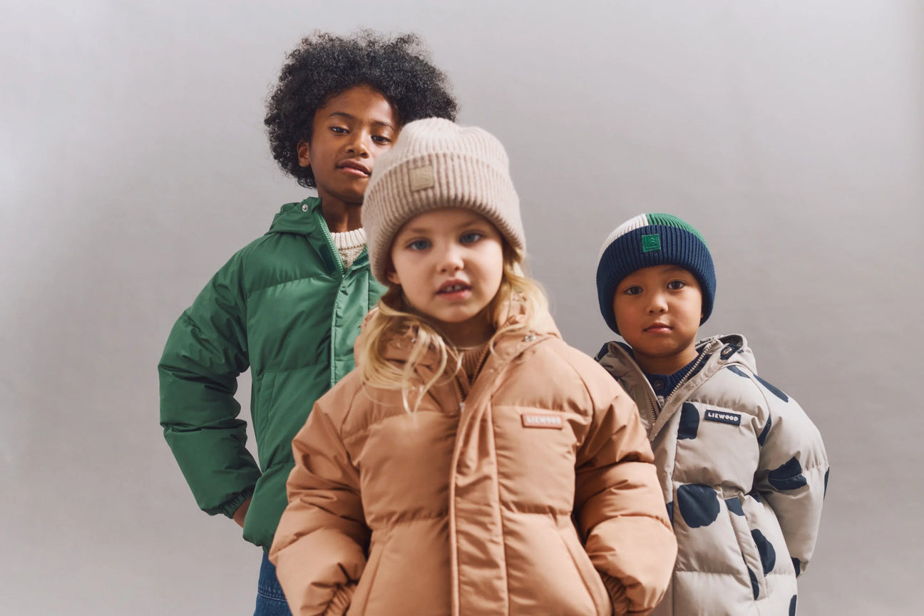 Drei Kinder in Liewood Winterjacken und Mützen vor neutralem Hintergrund, Kinder Mode Nook' d' Mel
