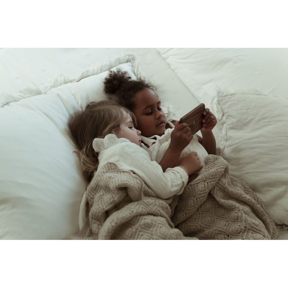 Zwei Kinder, die im Bett liegen und mit einer Babydecke 100 % Merinowolle gedeckt sind.